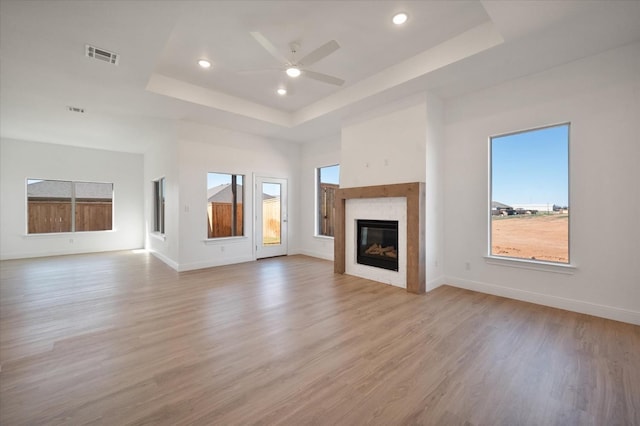 unfurnished living room with ceiling fan, a tray ceiling, and light hardwood / wood-style floors