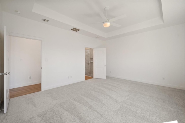 empty room with ceiling fan, light colored carpet, and a tray ceiling