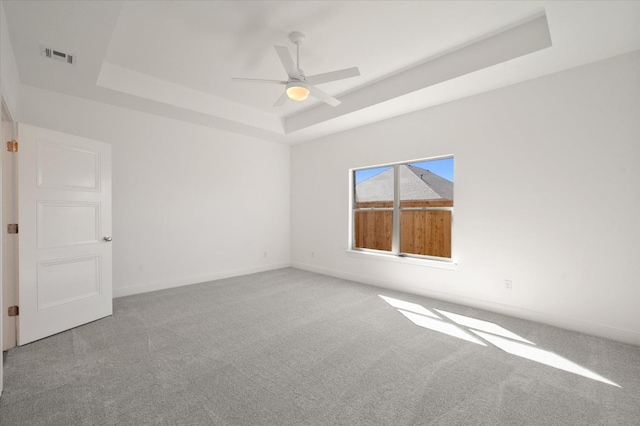 unfurnished room with a raised ceiling, ceiling fan, and carpet flooring