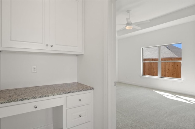 kitchen with white cabinetry, built in desk, ceiling fan, light colored carpet, and light stone countertops