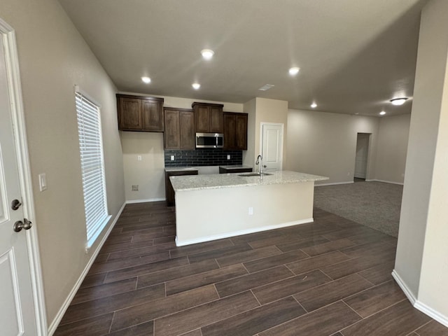 kitchen with light stone counters, sink, an island with sink, and backsplash