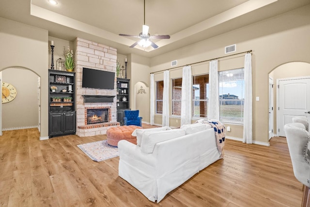 living room with ceiling fan, light hardwood / wood-style flooring, a fireplace, and a tray ceiling