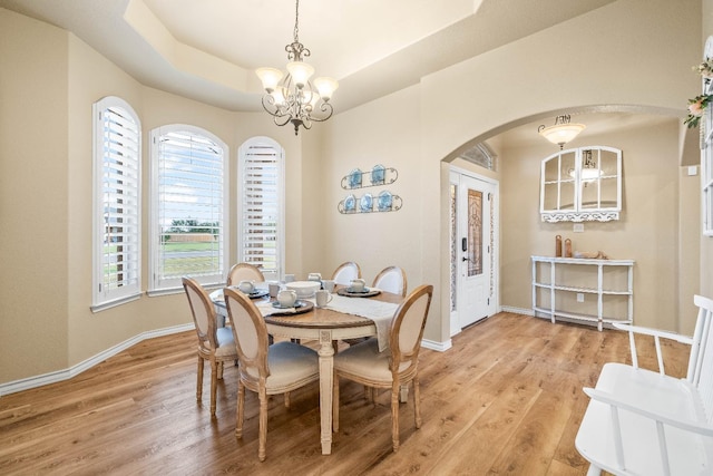 dining space featuring a tray ceiling, a chandelier, and light hardwood / wood-style flooring