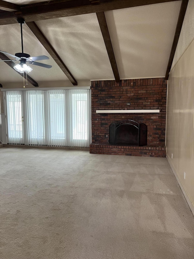 unfurnished living room featuring a ceiling fan, carpet floors, vaulted ceiling with beams, a textured ceiling, and a brick fireplace