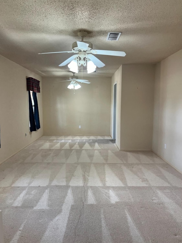 empty room featuring a ceiling fan, light colored carpet, visible vents, and a textured ceiling