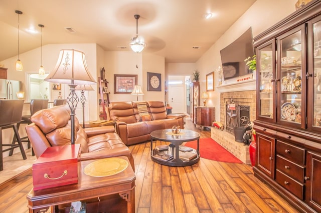 living room featuring vaulted ceiling, a brick fireplace, and light hardwood / wood-style flooring