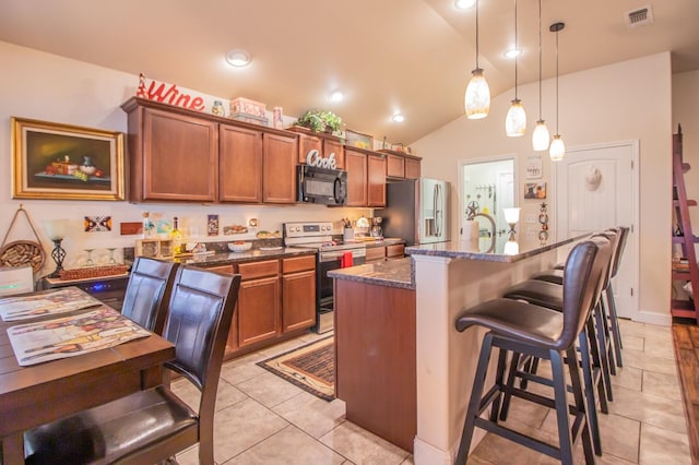 kitchen with lofted ceiling, a breakfast bar area, decorative light fixtures, a center island with sink, and stainless steel appliances