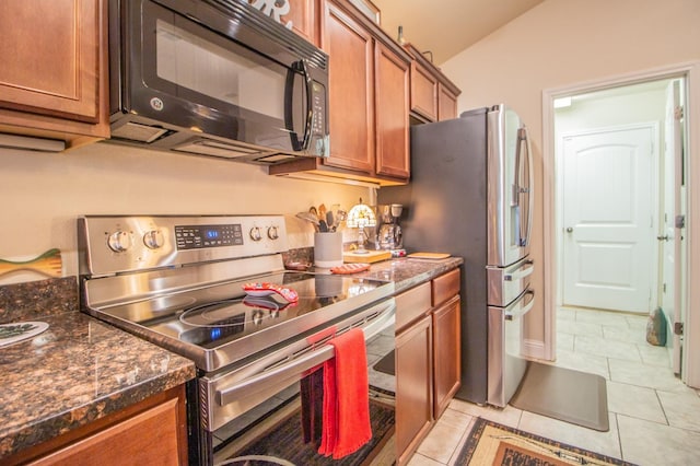 kitchen with dark stone countertops, lofted ceiling, appliances with stainless steel finishes, and light tile patterned floors