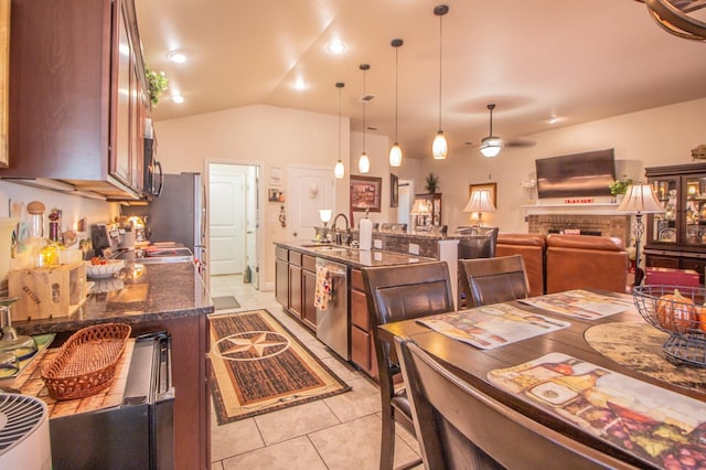 kitchen featuring vaulted ceiling, decorative light fixtures, dishwasher, sink, and dark stone counters