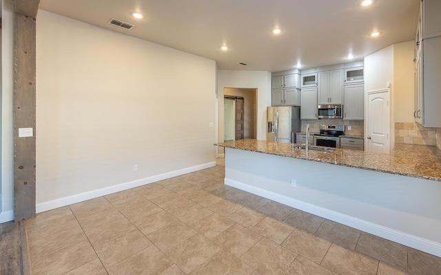 kitchen featuring sink, appliances with stainless steel finishes, decorative backsplash, kitchen peninsula, and dark stone counters