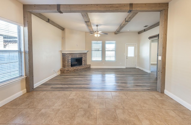 unfurnished living room featuring beam ceiling, a fireplace, ceiling fan, and light wood-type flooring