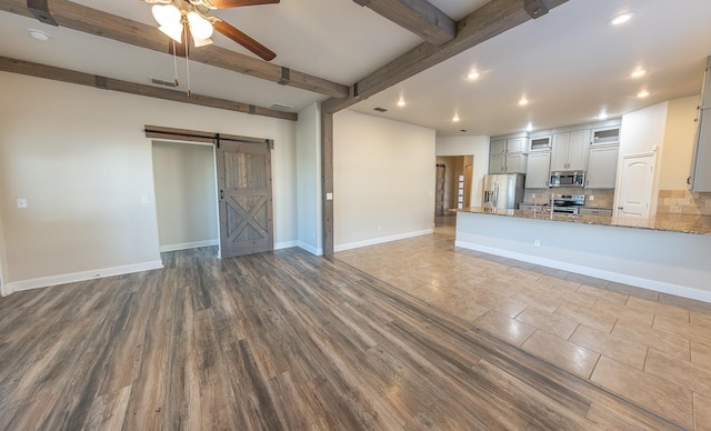 unfurnished living room with ceiling fan, wood-type flooring, a barn door, and beam ceiling