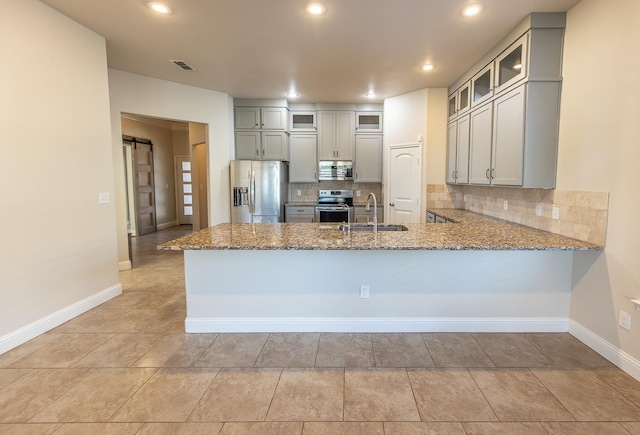 kitchen featuring gray cabinets, a barn door, kitchen peninsula, and appliances with stainless steel finishes