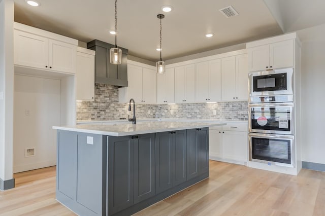 kitchen with a kitchen island with sink, hanging light fixtures, white cabinetry, light hardwood / wood-style floors, and built in microwave