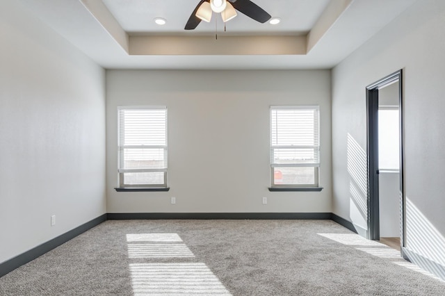 unfurnished room featuring ceiling fan, light colored carpet, plenty of natural light, and a tray ceiling