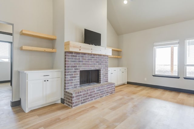 unfurnished living room featuring high vaulted ceiling, a brick fireplace, and light hardwood / wood-style flooring