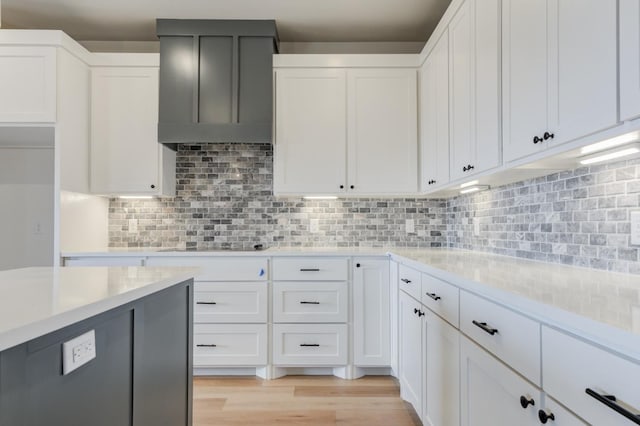 kitchen with white cabinetry, wall chimney exhaust hood, tasteful backsplash, and light hardwood / wood-style flooring