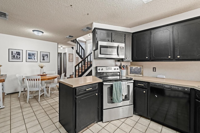 kitchen with light tile patterned floors, stainless steel appliances, kitchen peninsula, and a textured ceiling