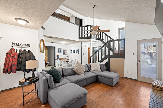 living room with ceiling fan, hardwood / wood-style flooring, high vaulted ceiling, and a textured ceiling