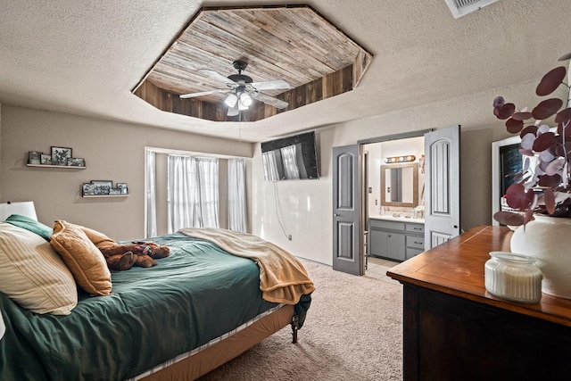 bedroom featuring connected bathroom, light colored carpet, a textured ceiling, a tray ceiling, and ceiling fan