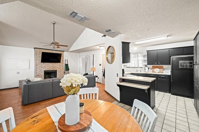 dining space featuring sink, vaulted ceiling, a brick fireplace, a textured ceiling, and ceiling fan