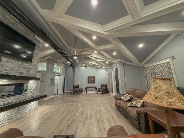 living room with ceiling fan, a stone fireplace, lofted ceiling with beams, and light wood-type flooring