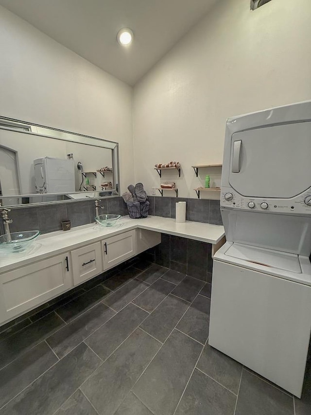 laundry room featuring stacked washer / dryer, sink, and dark tile patterned floors