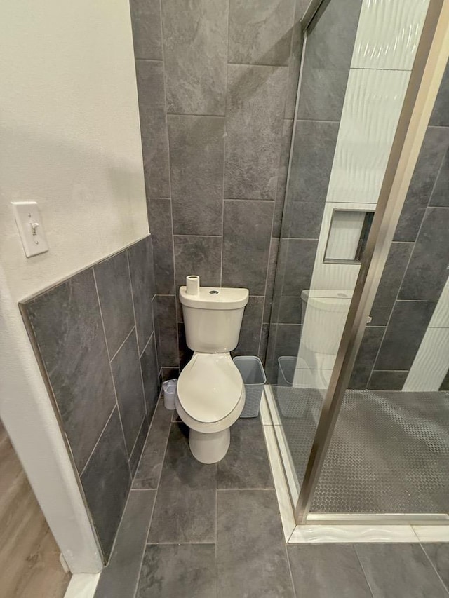 bathroom featuring tile walls, tile patterned floors, toilet, and tiled shower