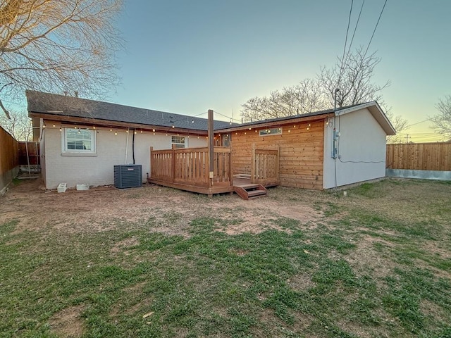 back house at dusk featuring a wooden deck, a lawn, and central air condition unit