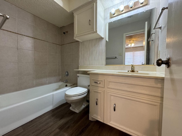 full bathroom with tiled shower / bath combo, vanity, wood-type flooring, a textured ceiling, and toilet