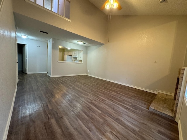 unfurnished living room featuring a towering ceiling, dark wood-type flooring, and a textured ceiling