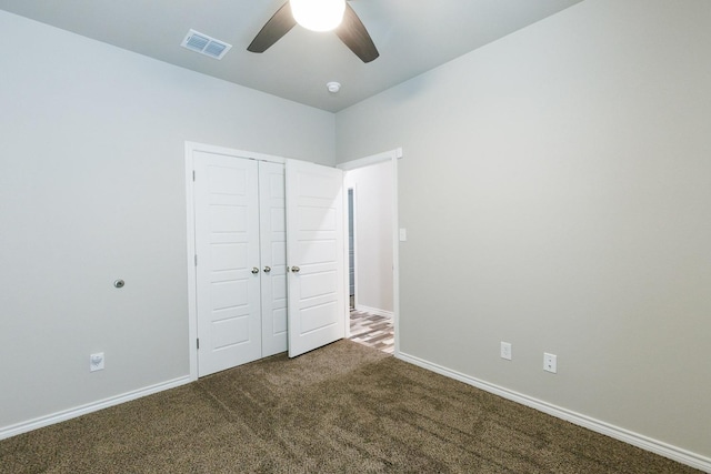 unfurnished bedroom with ceiling fan, dark carpet, and a closet