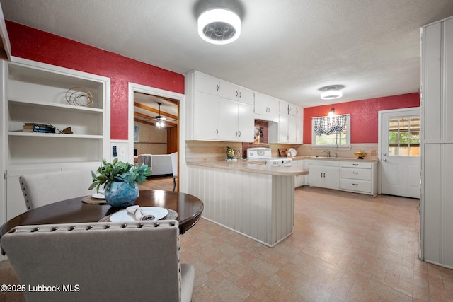 2005 32nd St, Lubbock, TX 79411 - kitchen with stove, a sink, a peninsula, light countertops, and white cabinets