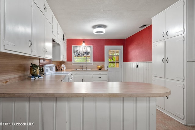 2005 32nd St, Lubbock, TX 79411 - kitchen featuring white range oven, a peninsula, a sink, light countertops, and a wainscoted wall