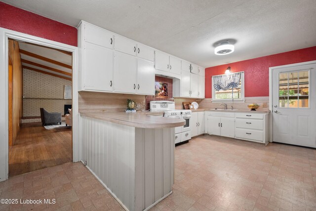 2005 32nd St, Lubbock, TX 79411 - kitchen with white range, light countertops, white cabinets, a peninsula, and a sink
