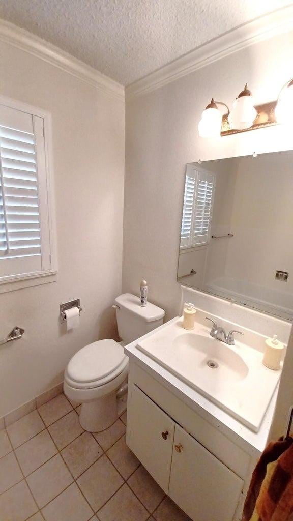 bathroom featuring toilet, a textured ceiling, ornamental molding, vanity, and tile patterned flooring