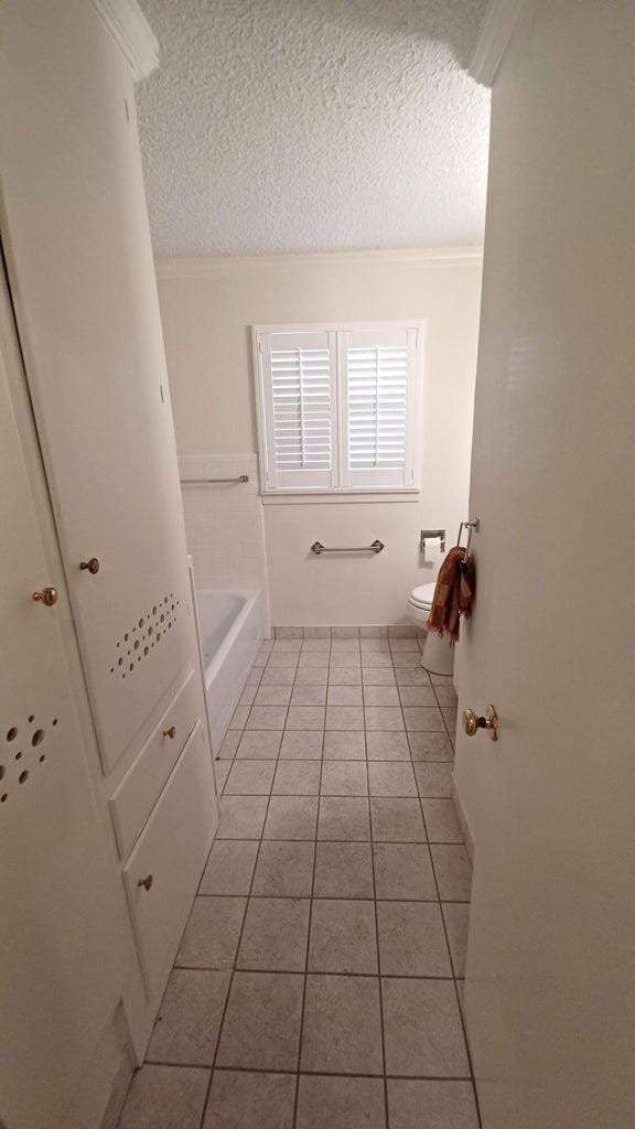 bathroom with tile patterned flooring, a washtub, a textured ceiling, and toilet