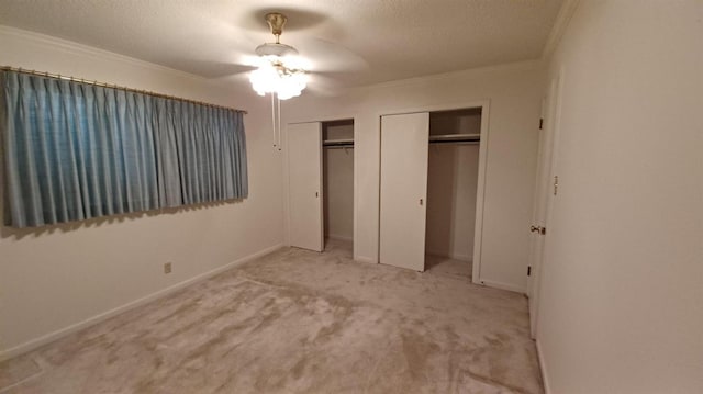 unfurnished bedroom with crown molding, a textured ceiling, light carpet, and two closets