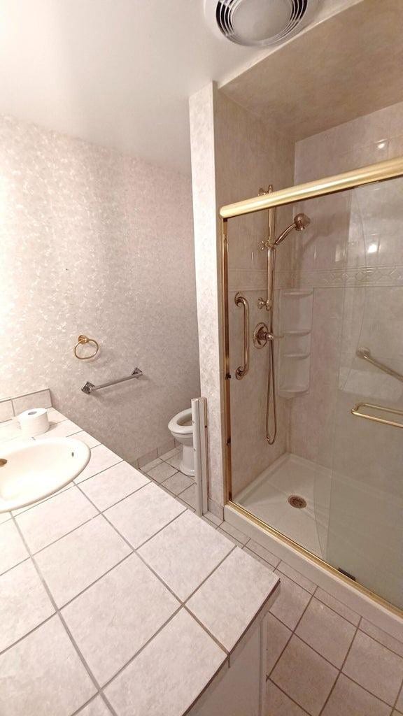 bathroom featuring tile patterned flooring, toilet, a shower with shower door, and sink