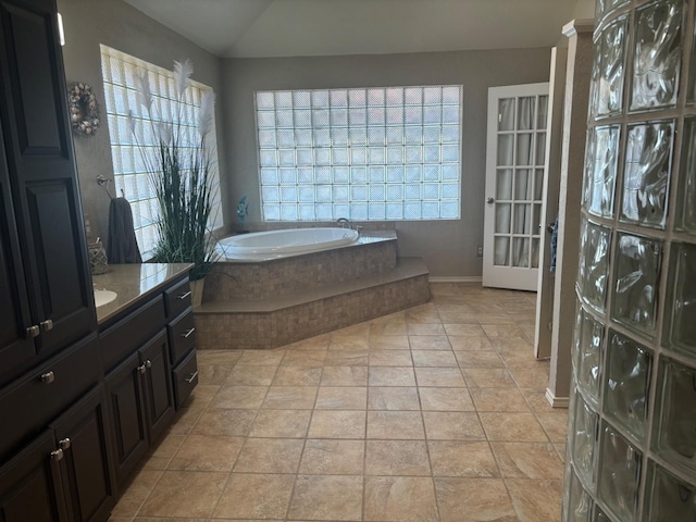 bathroom featuring tiled tub, vanity, a wealth of natural light, vaulted ceiling, and tile patterned floors