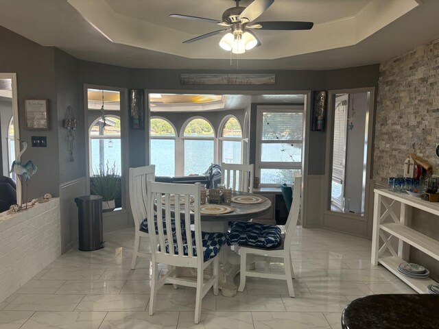 dining room featuring ceiling fan, a healthy amount of sunlight, and a tray ceiling