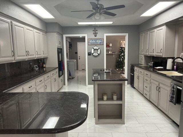 kitchen featuring sink, a center island, dark stone countertops, dishwasher, and ceiling fan