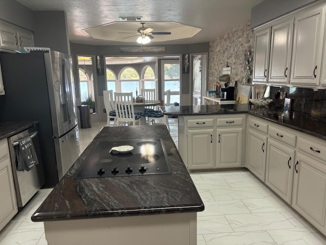 kitchen with dishwasher, black stovetop, a raised ceiling, a kitchen island, and dark stone counters