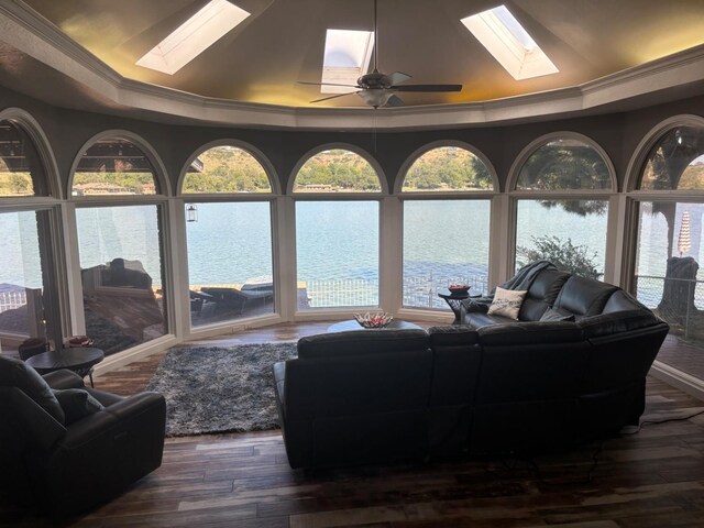 living room with a raised ceiling, ornamental molding, a water view, and a skylight