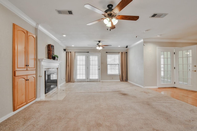 unfurnished living room with a premium fireplace, crown molding, light colored carpet, and ceiling fan