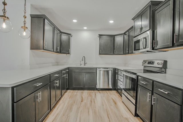 kitchen with sink, light hardwood / wood-style flooring, appliances with stainless steel finishes, hanging light fixtures, and kitchen peninsula