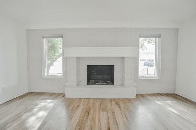 unfurnished living room with a healthy amount of sunlight, a brick fireplace, and light hardwood / wood-style flooring