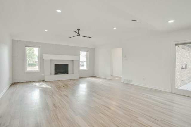 unfurnished living room featuring brick wall, a fireplace, ceiling fan, and light wood-type flooring