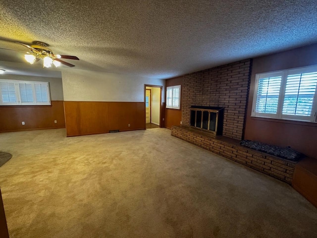 unfurnished living room featuring a brick fireplace, wooden walls, light colored carpet, and a textured ceiling