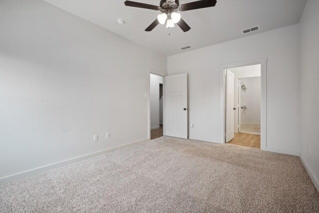 unfurnished bedroom featuring ensuite bathroom, light colored carpet, and ceiling fan